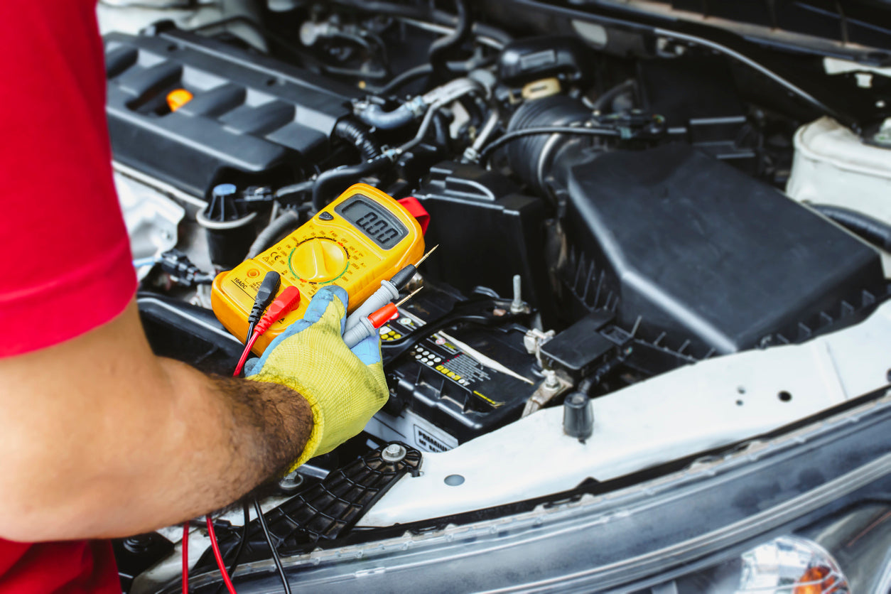 Auto electrician using yellow multimeter to test car battery